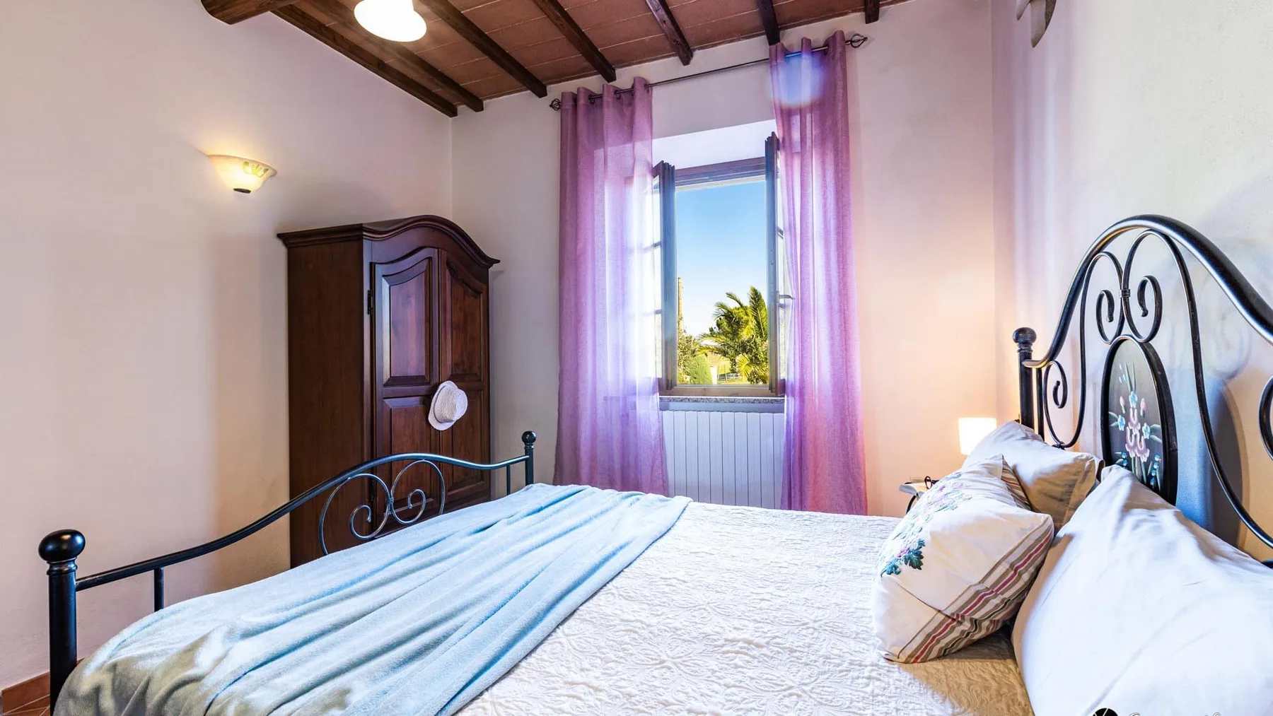 Un dormitorio con una cama grande, un armario oscuro y una ventana con cortinas moradas.