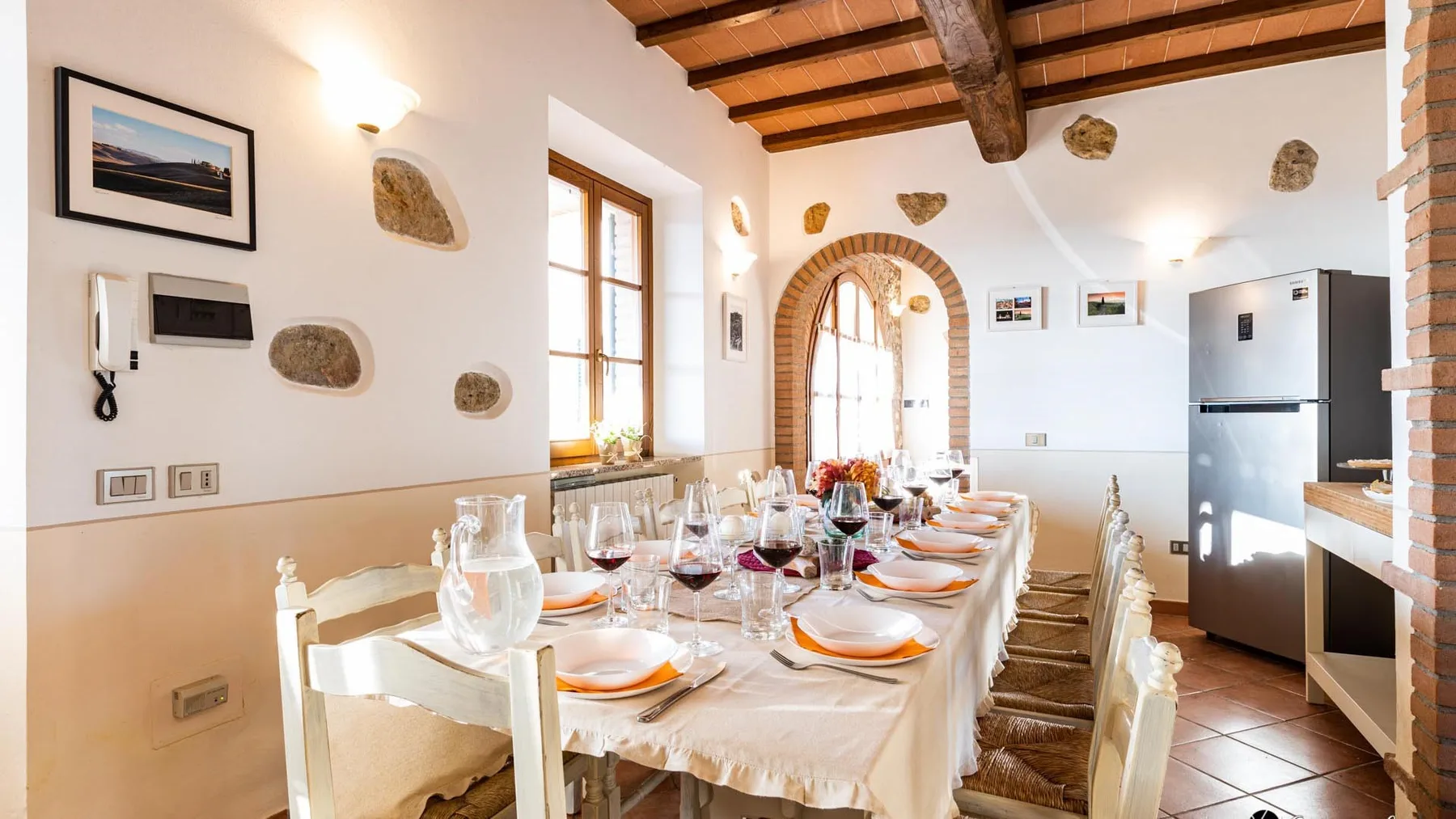 Un comedor luminoso con una mesa larga preparada para comer bajo vigas de madera a la vista.