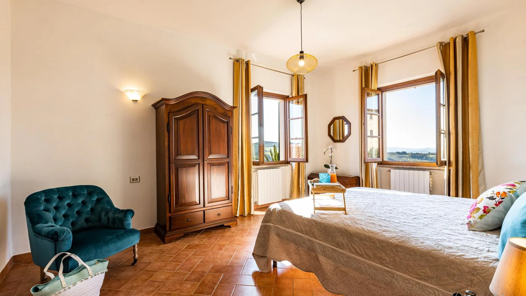 Un dormitorio luminoso con una cama grande, ventanas altas y un armario de madera.