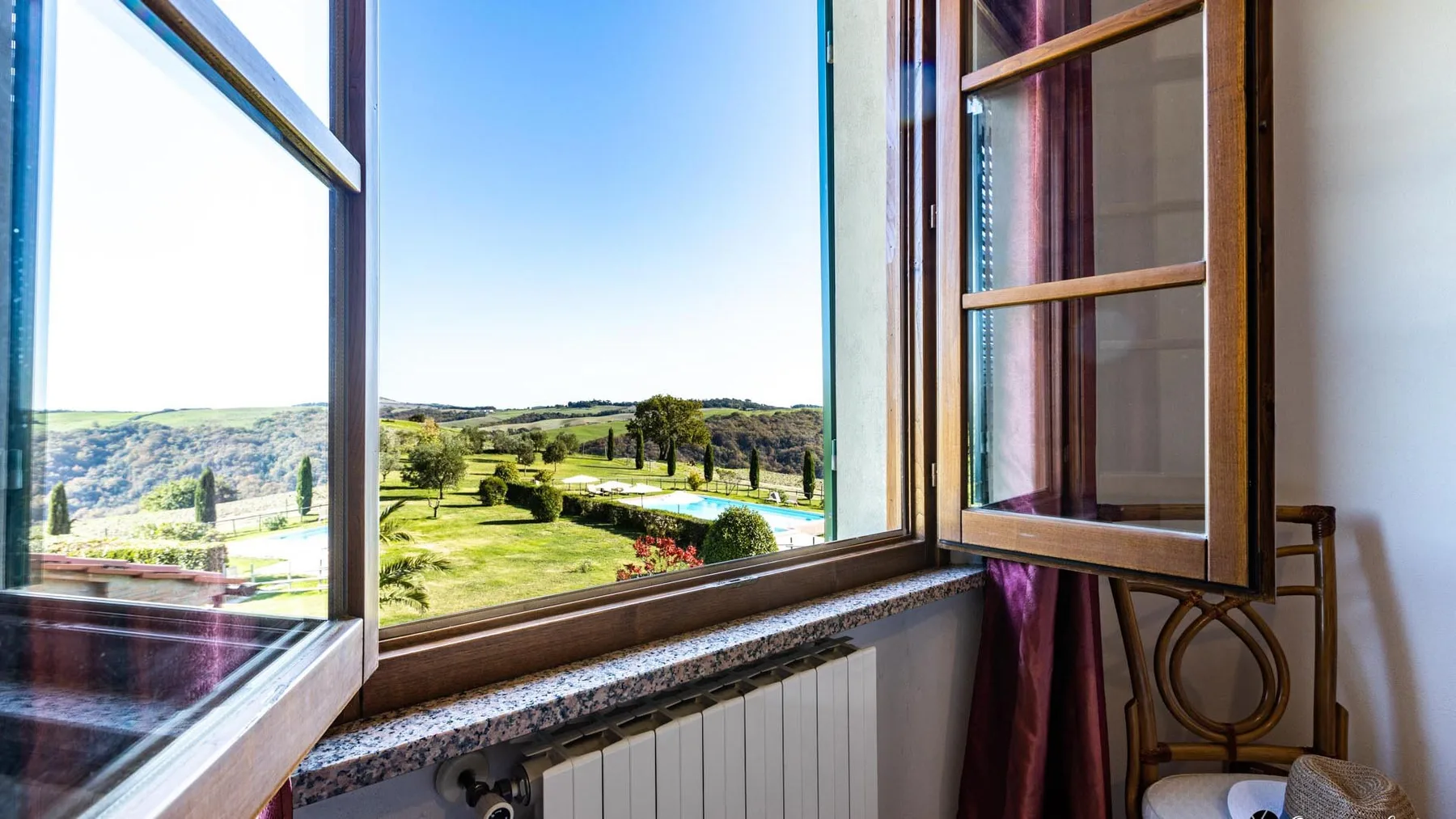 Una ventana abierta da a un paisaje verde de campo y colinas onduladas.