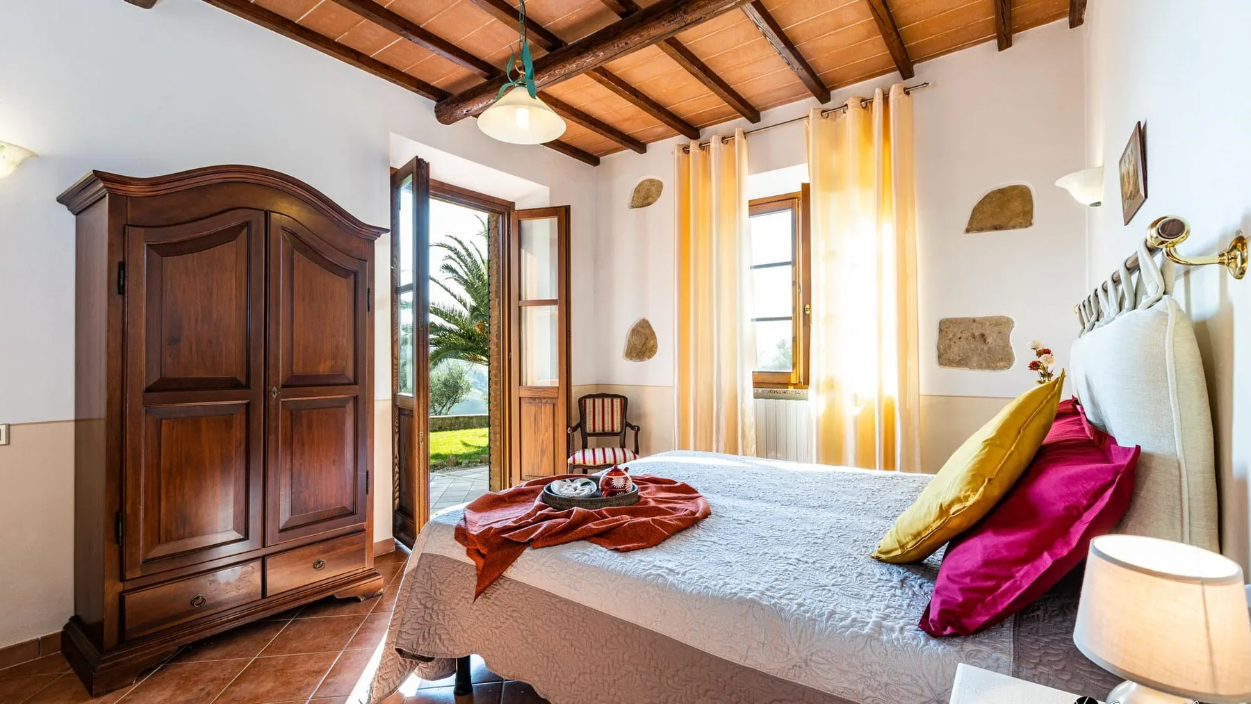 Un dormitorio luminoso con una cama grande, un armario de madera oscura y puertas abiertas al balcón.