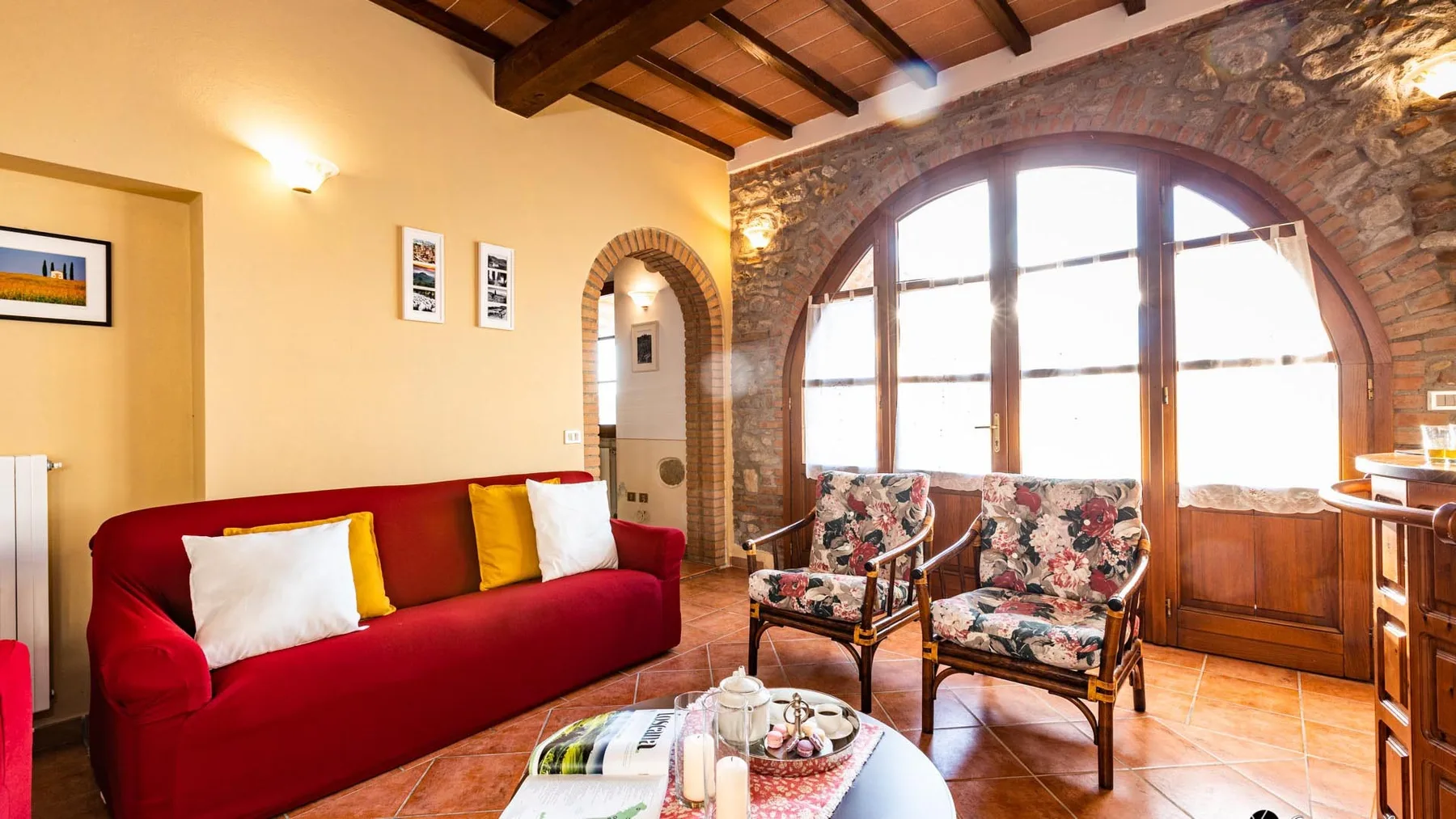 Una sala luminosa con un sofá rojo y sillones estampados junto a una gran ventana arqueada.