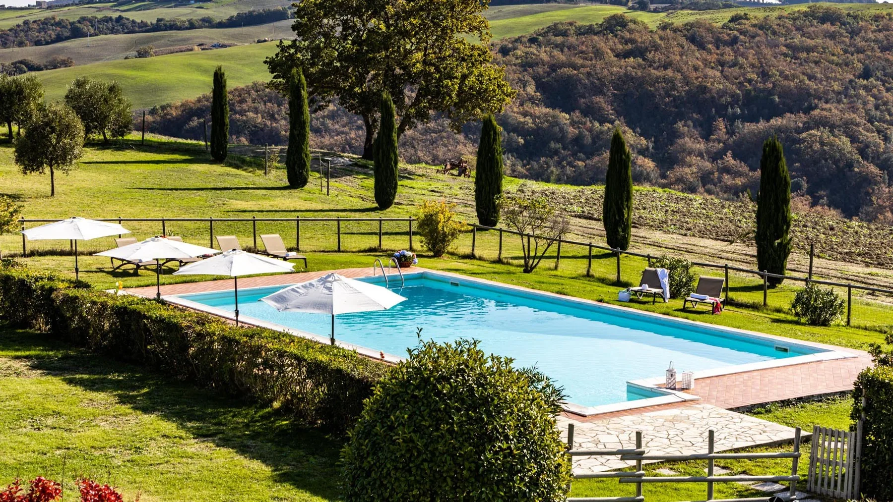 Una piscina al aire libre está junto a una ladera cubierta de césped y un paisaje boscoso.