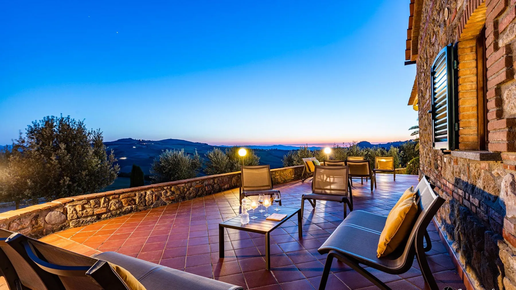 Una terraza al aire libre con asientos ofrece vistas a colinas al atardecer.