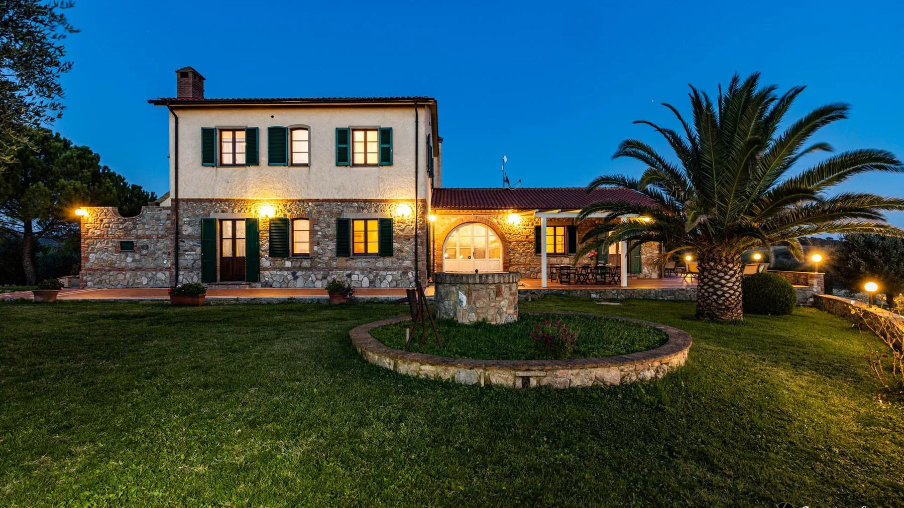 Una casa de dos plantas se alza detrás de un jardín circular al anochecer.