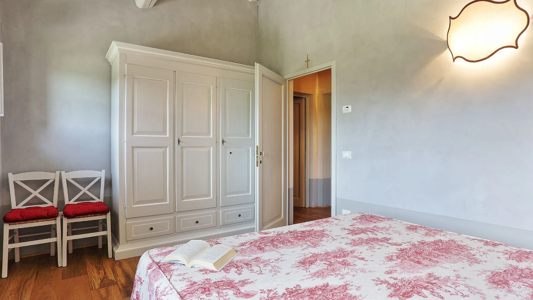 Un dormitorio con un armario grande, dos sillas y una colcha floral.