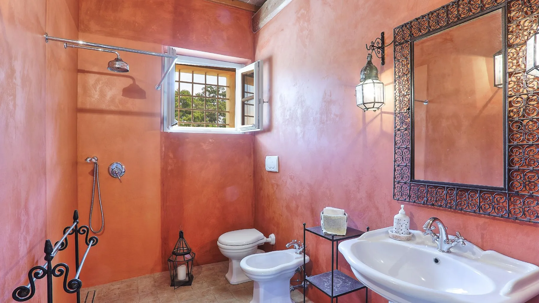 Un baño rosa con ducha, inodoro, bidé y lavabo bajo un espejo ornamentado.