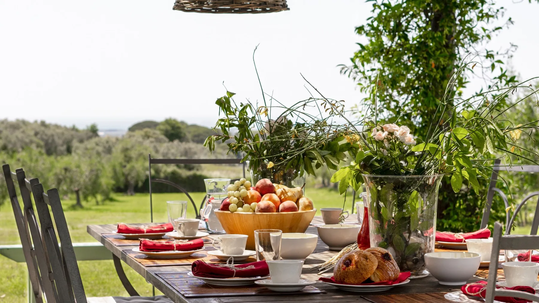 Una mesa de comedor al aire libre está puesta con platos, fruta y un ave asada.