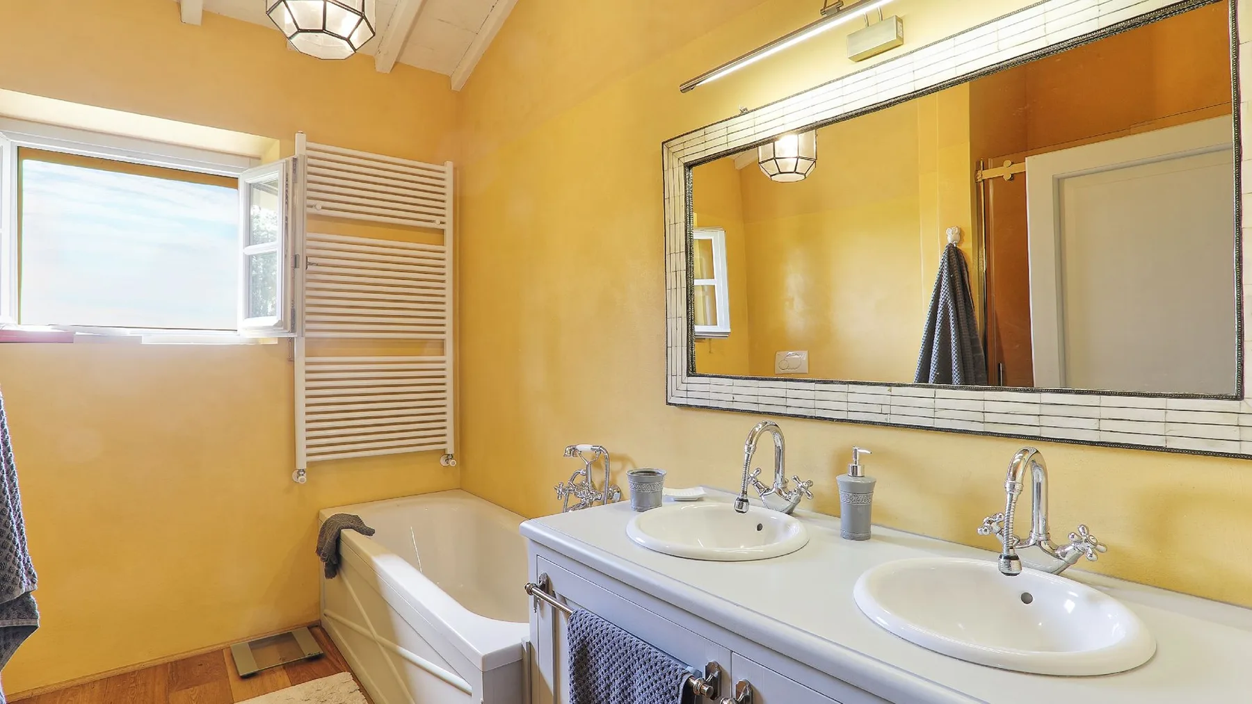 Un baño amarillo con bañera, dos lavabos y un gran espejo en la pared.