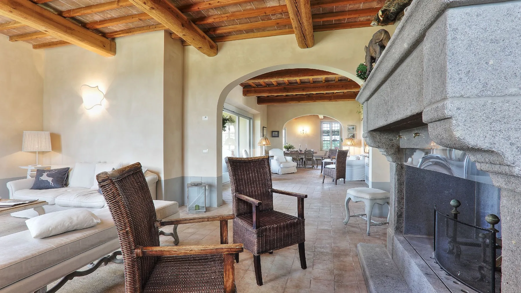 Una sala amplia con asientos de mimbre, una chimenea y un arco que da a otra zona de estar.