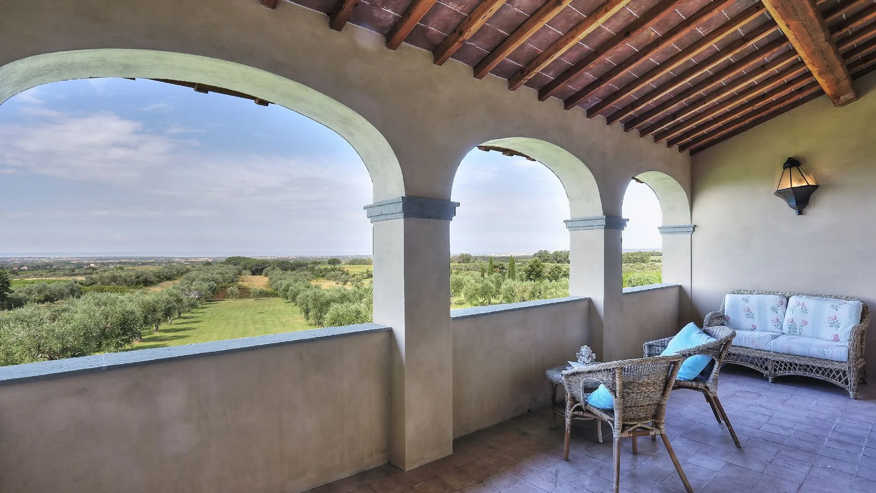Una terraza cubierta con arcos da a campos verdes y tiene asientos cerca.