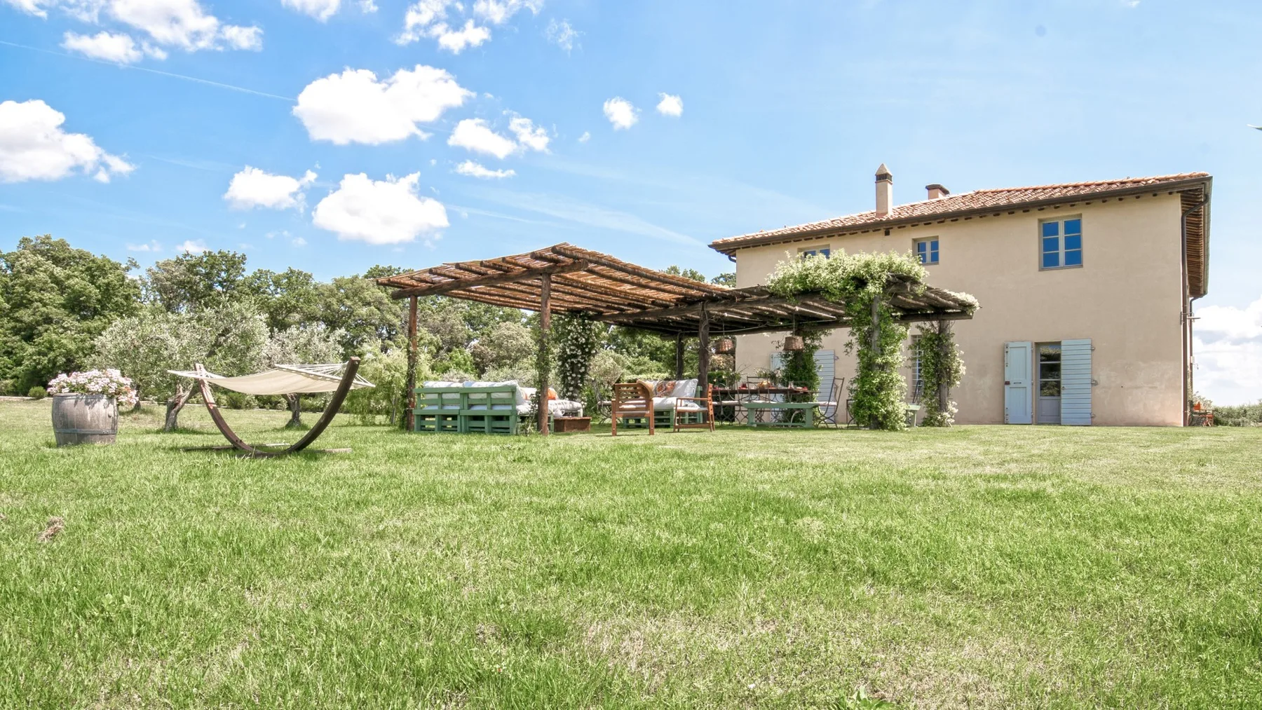 Un patio con césped, una pérgola y una casa bajo un cielo azul.