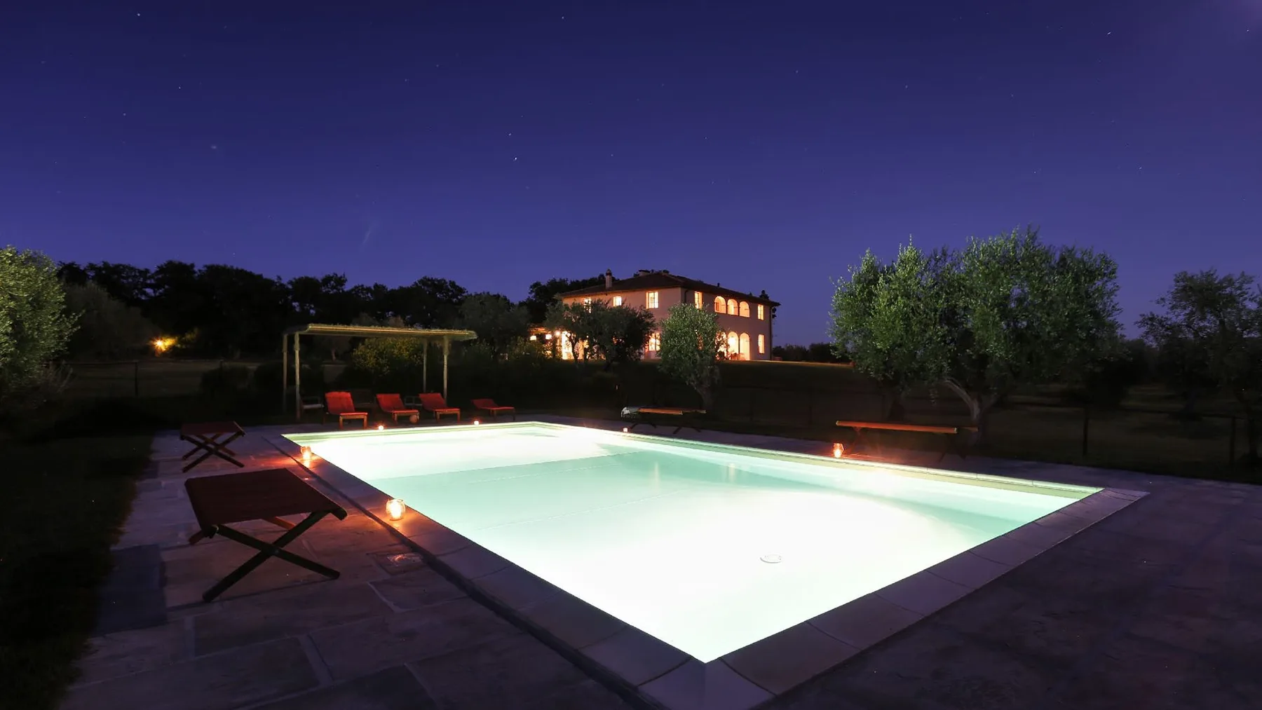 Una piscina exterior iluminada se ve bajo un cielo nocturno estrellado.