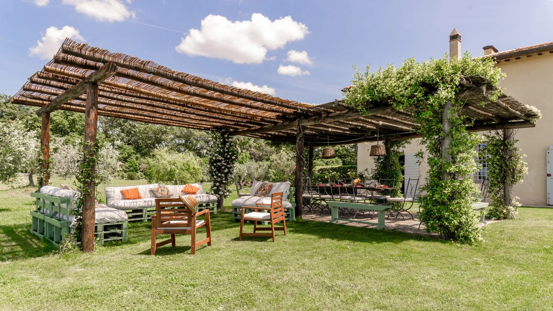 Un patio ajardinado con una pérgola de madera y asientos al aire libre junto a una casa.