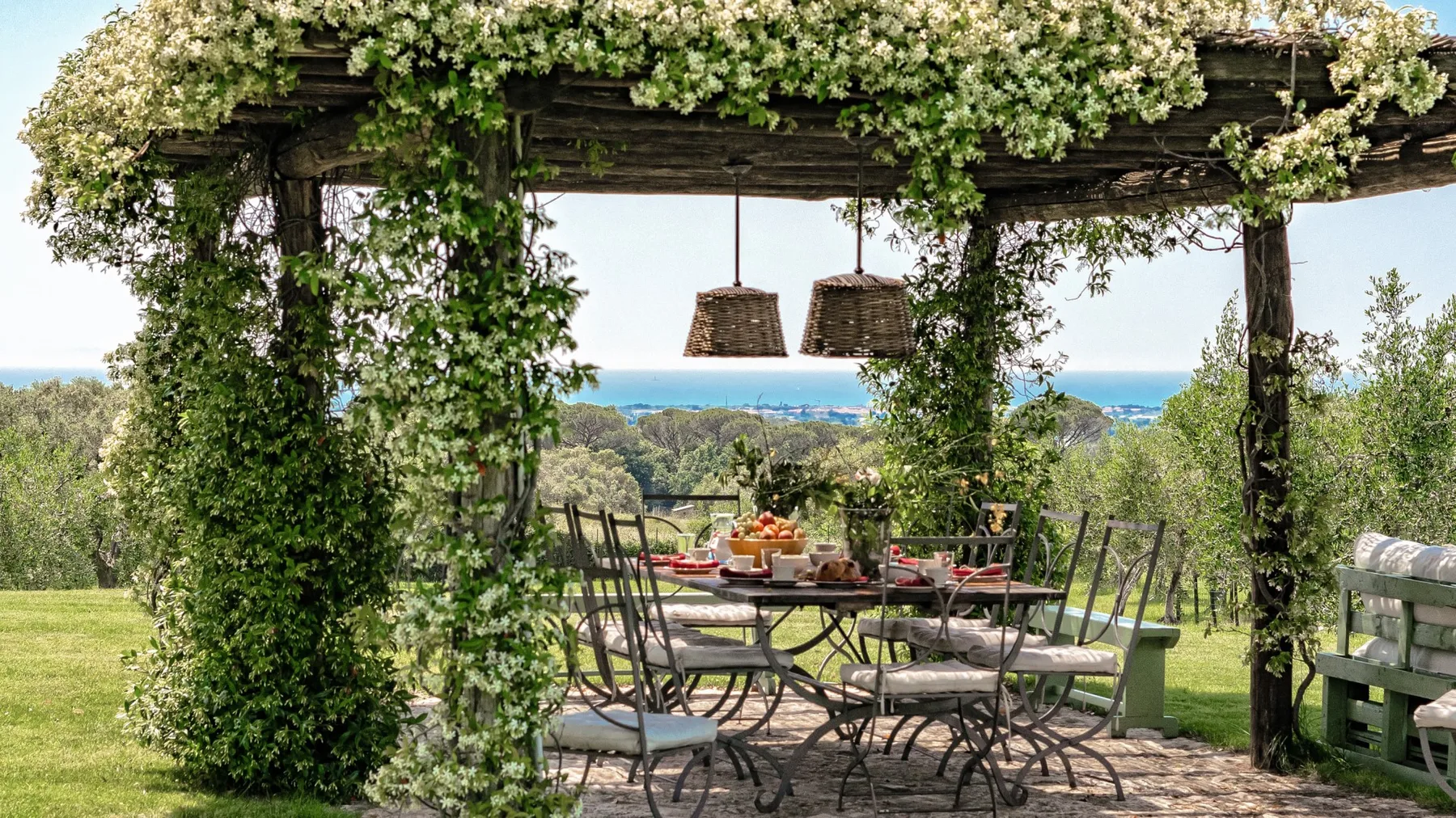 Un comedor al aire libre bajo una pérgola cubierta de enredaderas, con mesa y sillas frente a la vegetación.