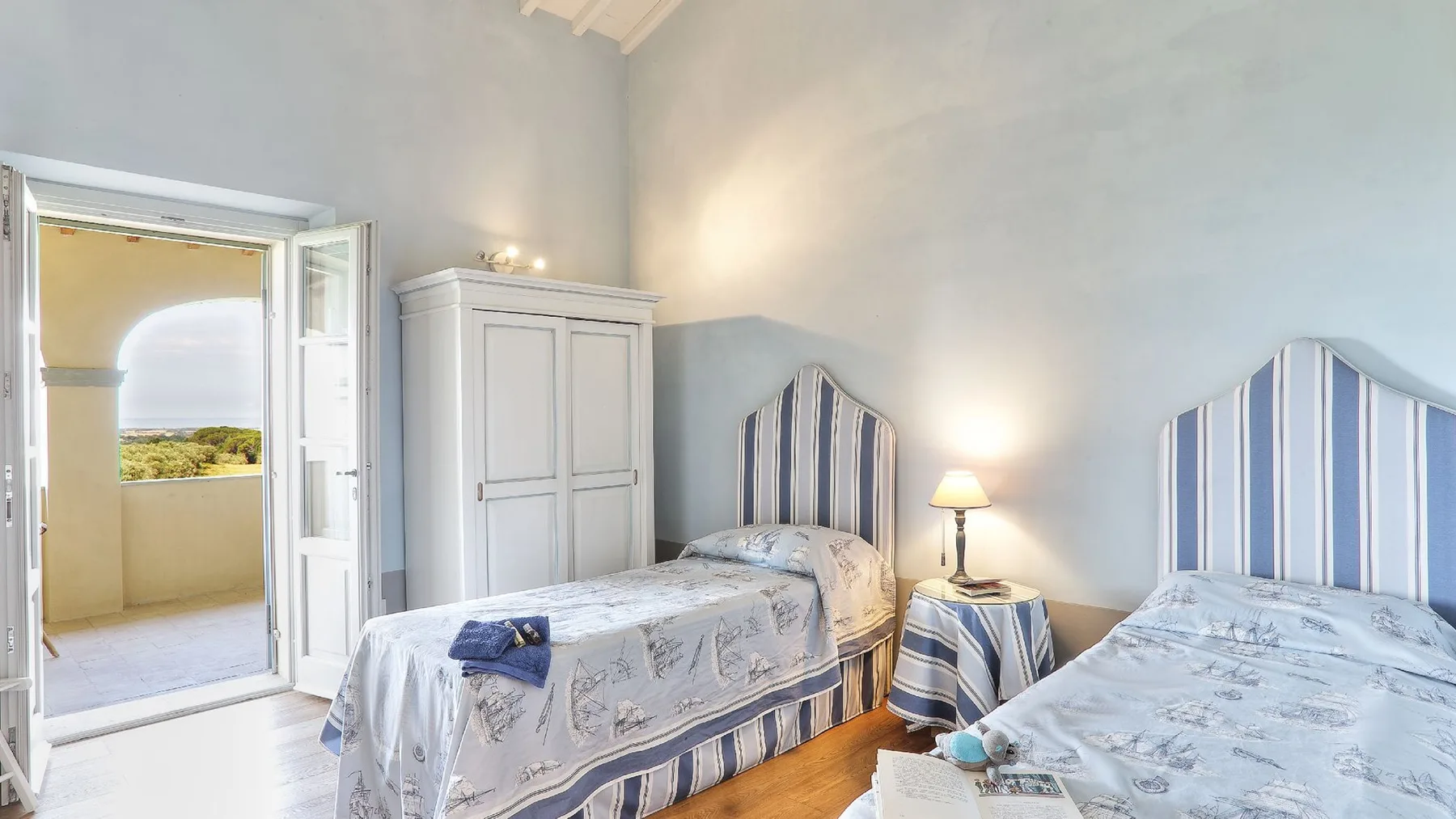 Un dormitorio luminoso con dos camas y una puerta abierta a un balcón.