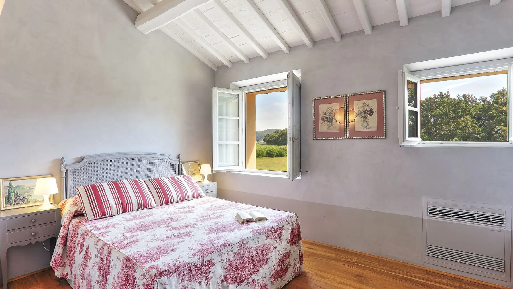 Un dormitorio con una cama bajo dos ventanas abiertas.