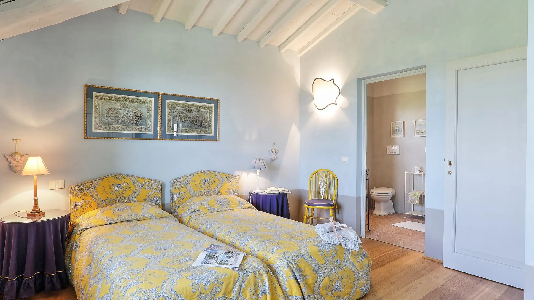 Un dormitorio con dos camas cubiertas con ropa de cama amarilla estampada y cuadros enmarcados.