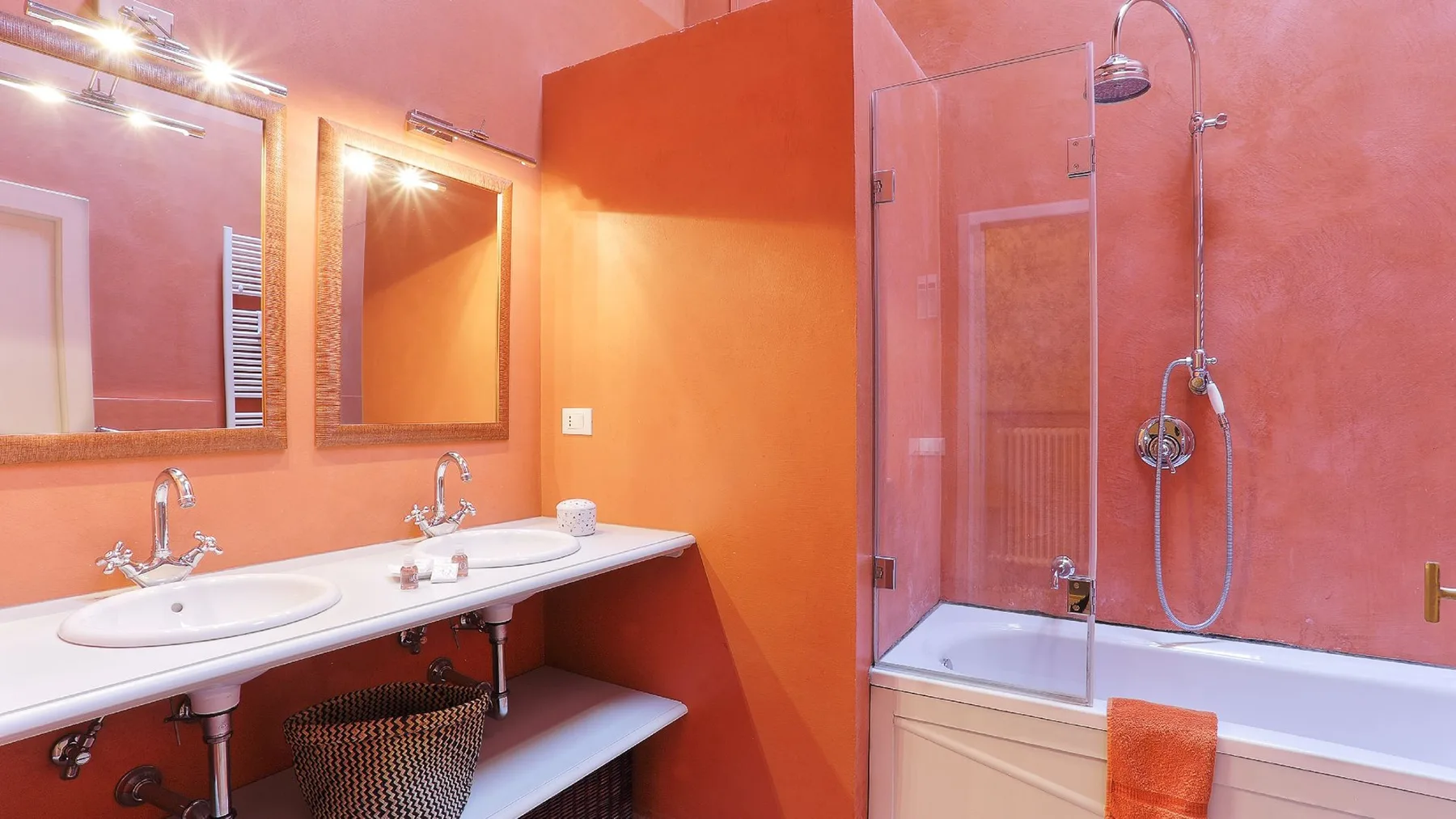 Un baño naranja con una encimera larga con lavabos y una ducha con mampara de vidrio.