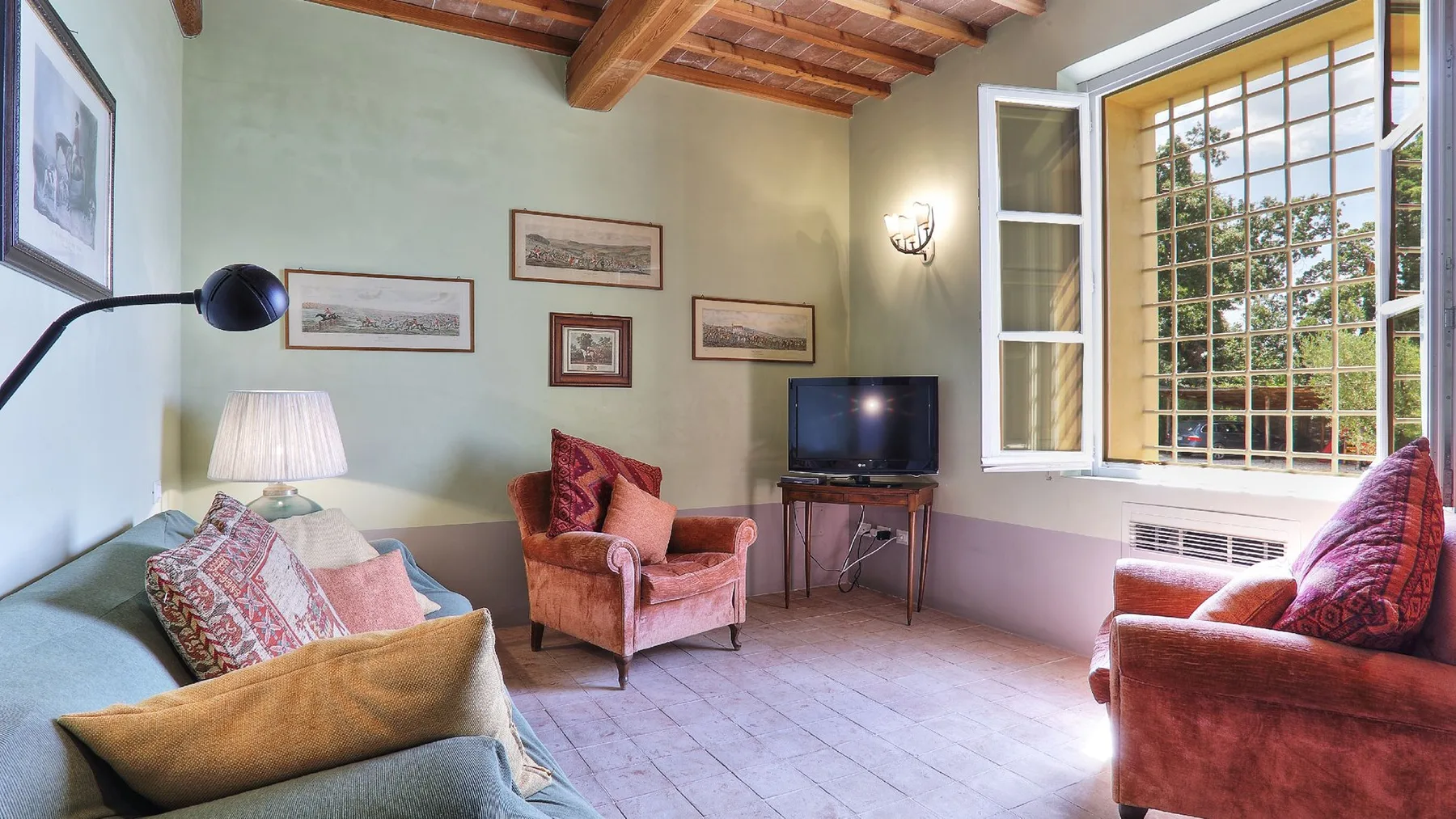 Una sala de estar con asientos acolchados, cuadros enmarcados y una ventana grande.