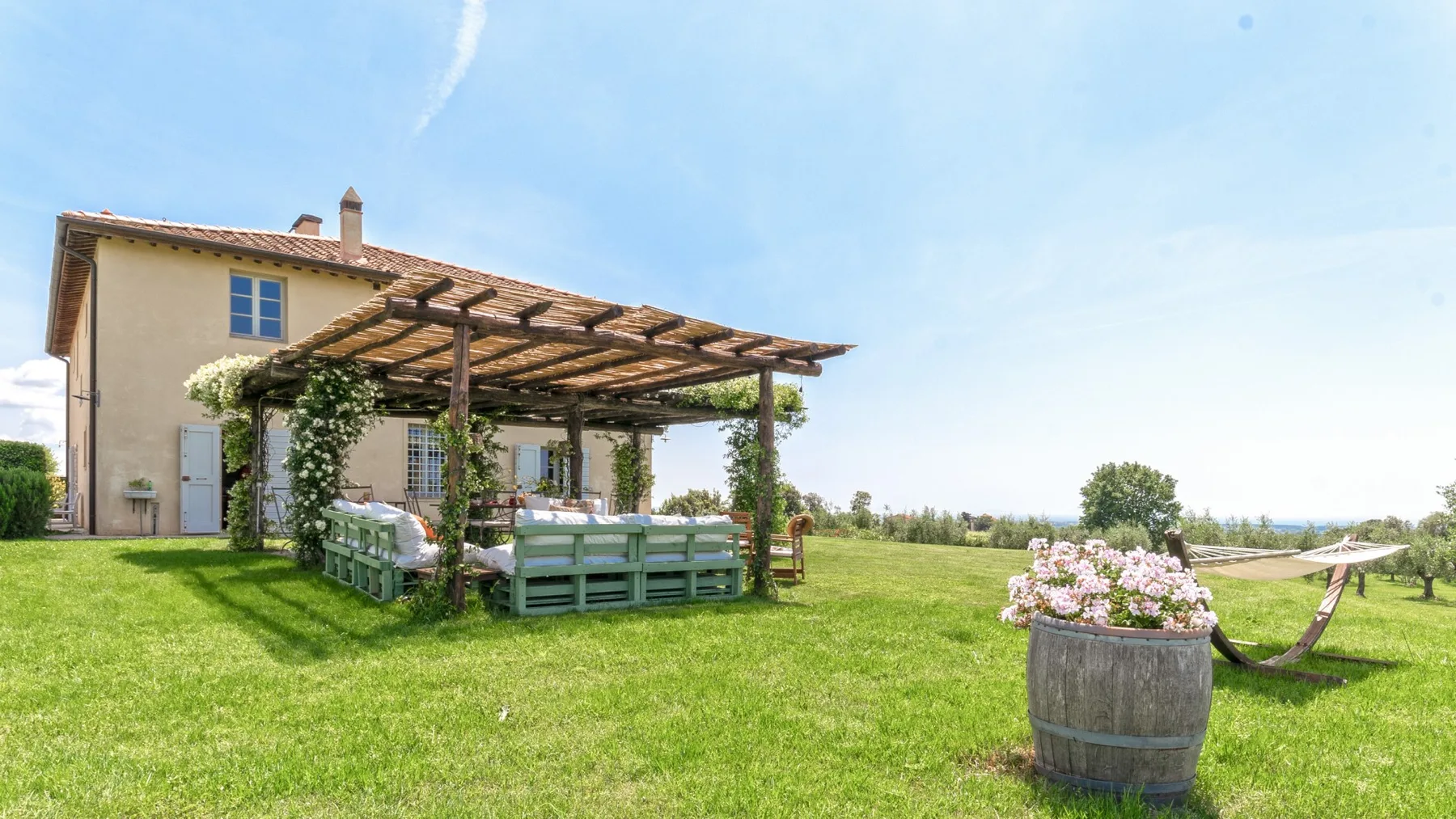 Un jardín con césped y una pérgola de madera que da sombra a una zona de estar.