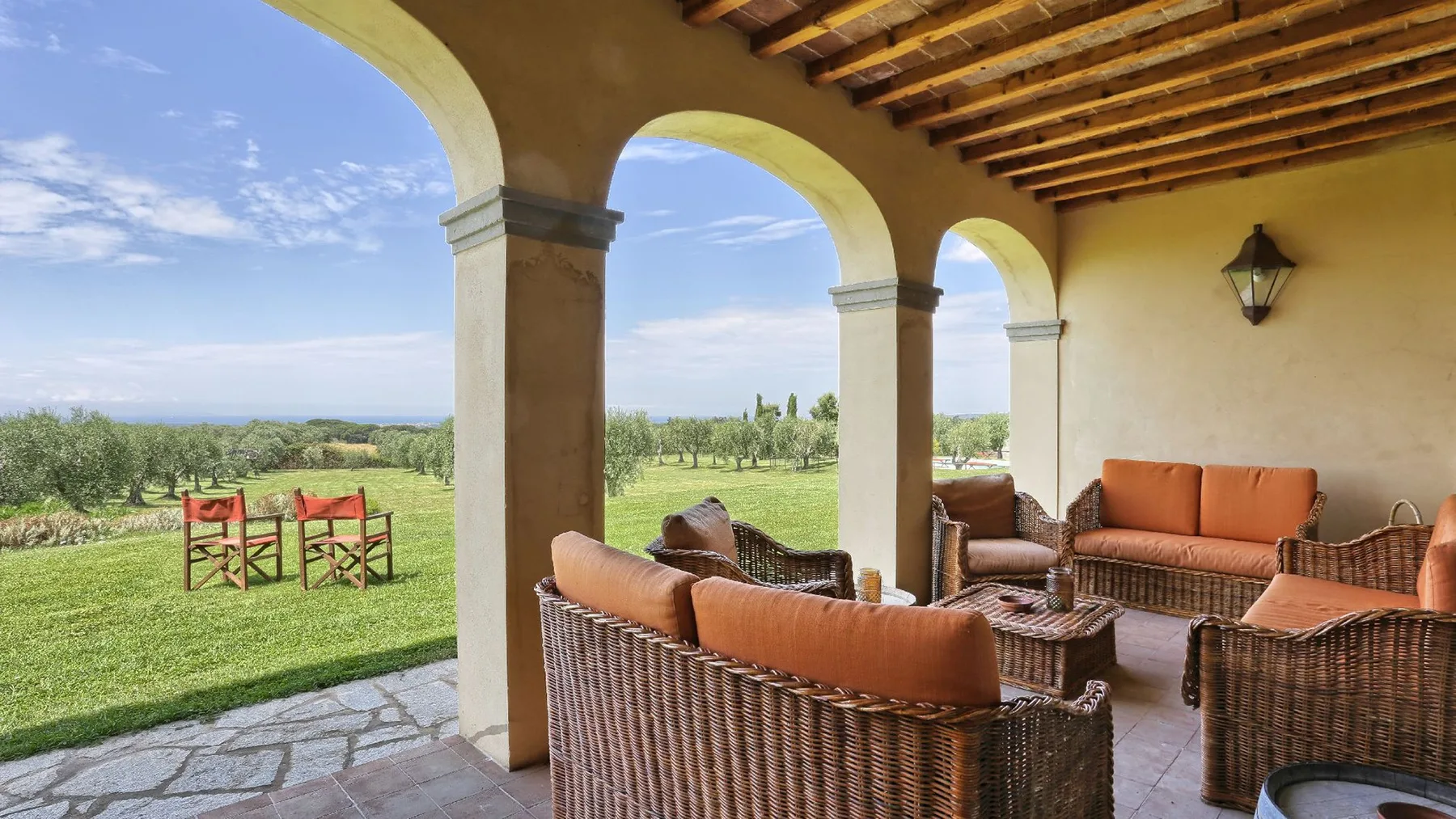 Una zona de estar cubierta al aire libre con muebles de mimbre da a un campo verde.
