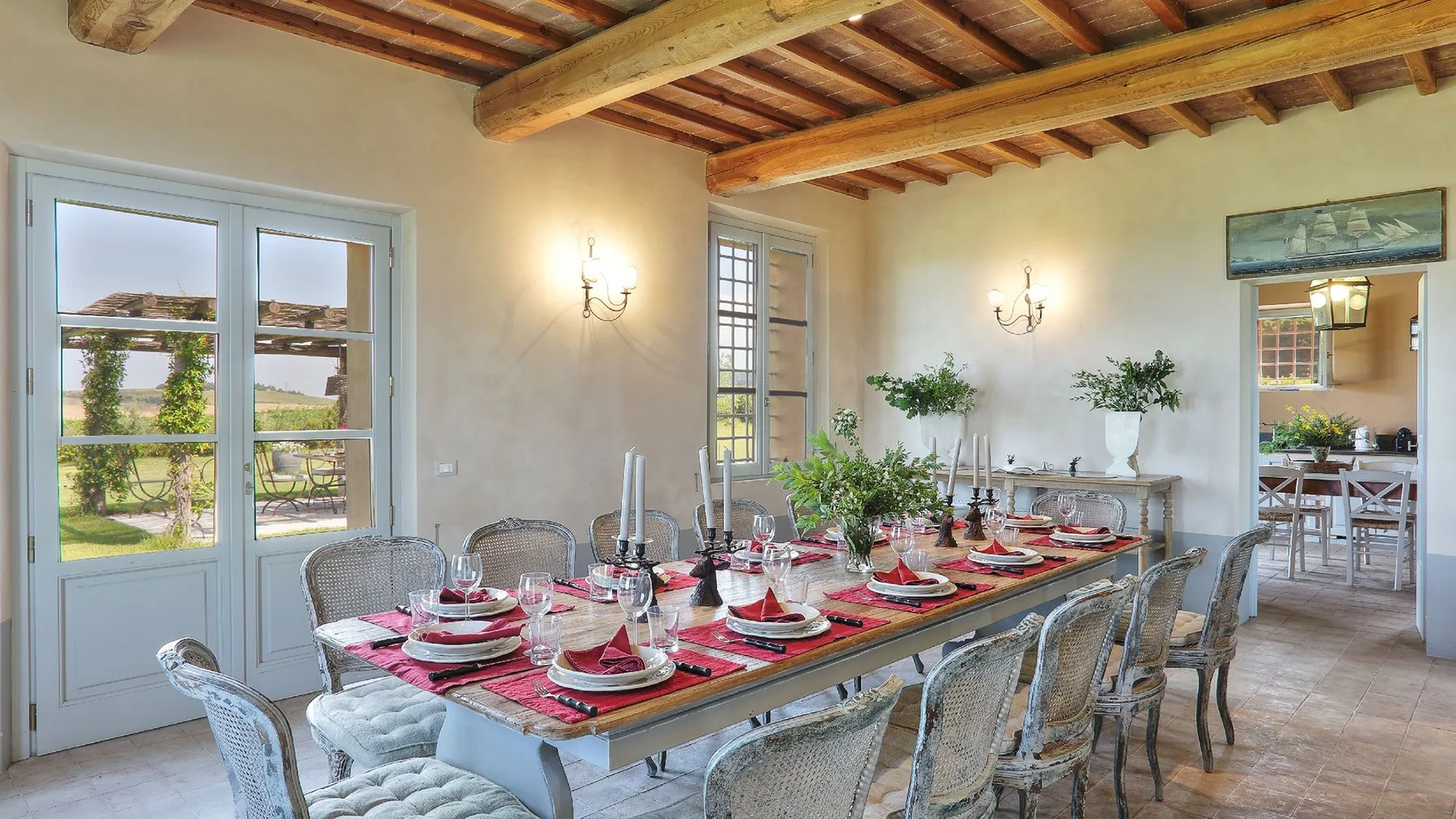 Un comedor con una mesa larga preparada con manteles individuales rojos y vajilla.