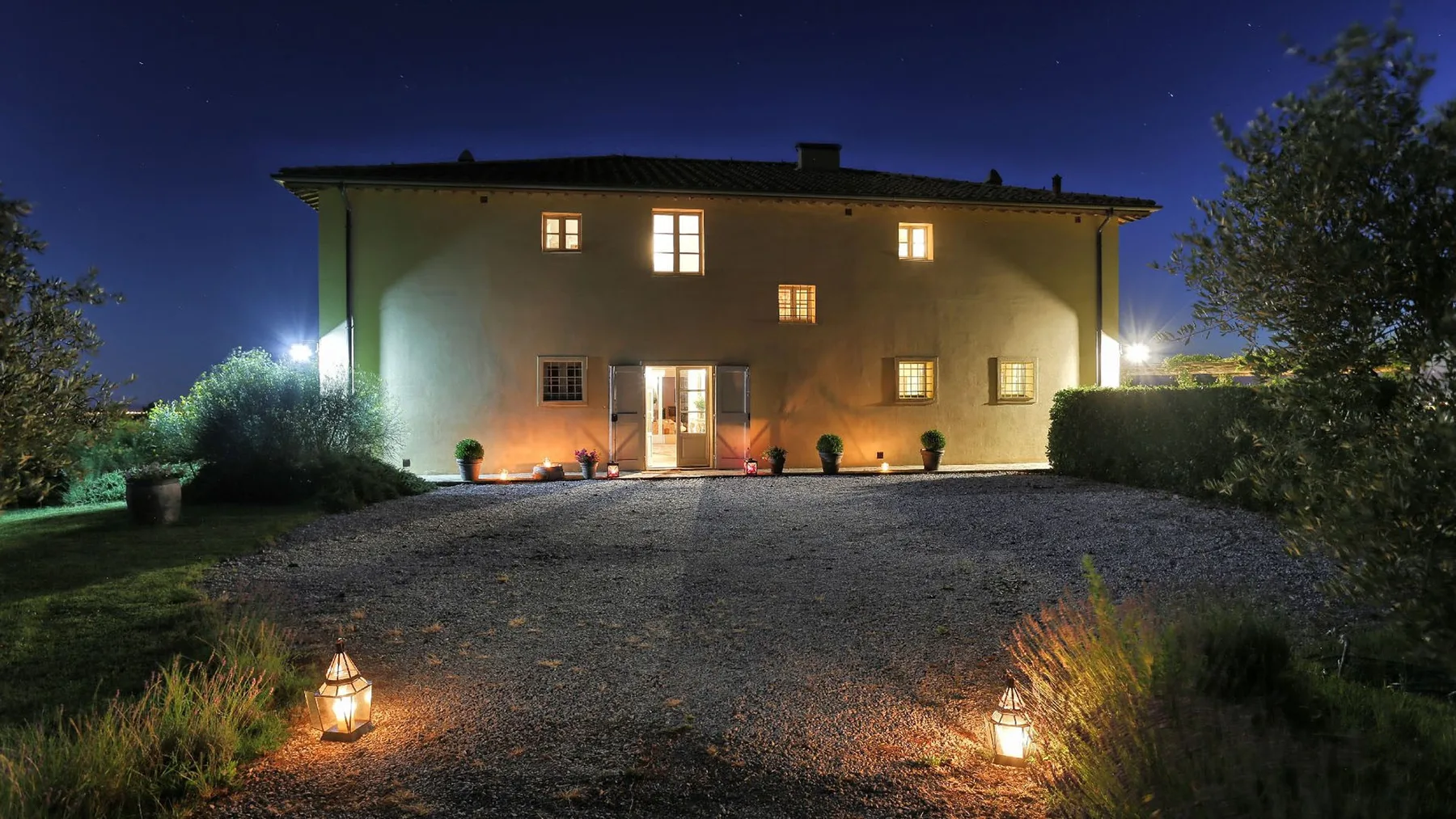 Una casa iluminada de noche junto a una entrada de grava y un jardín.