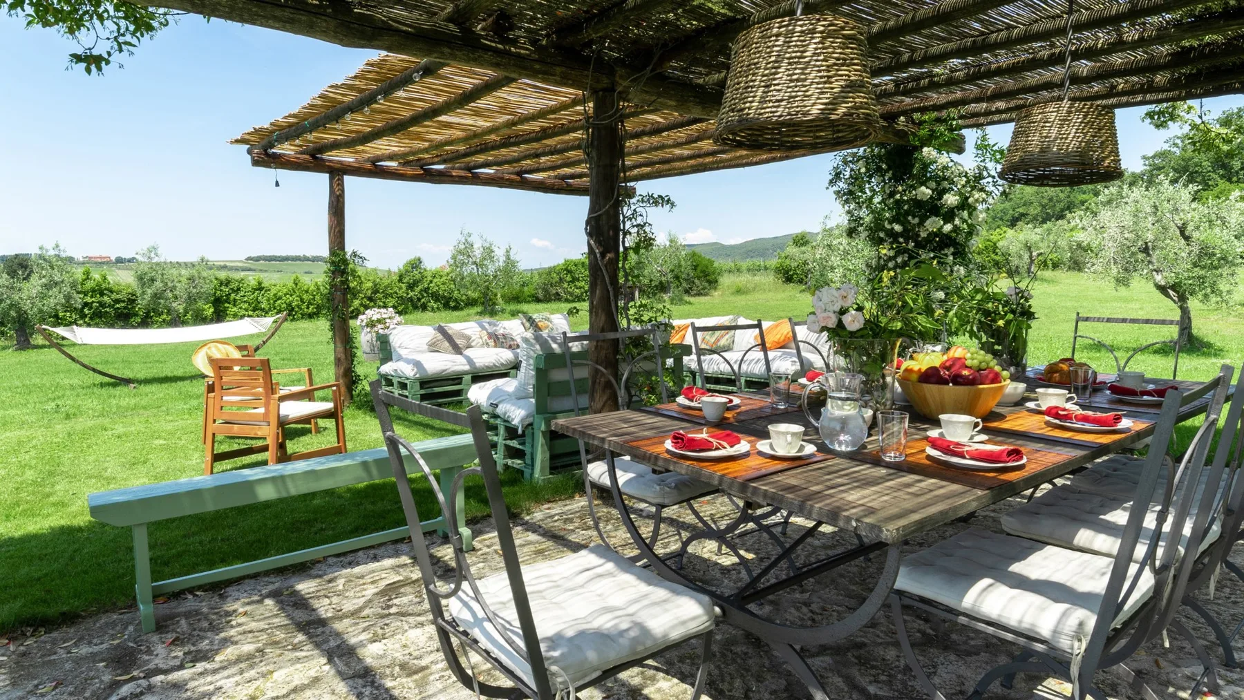Un comedor al aire libre con la mesa puesta bajo una pérgola.