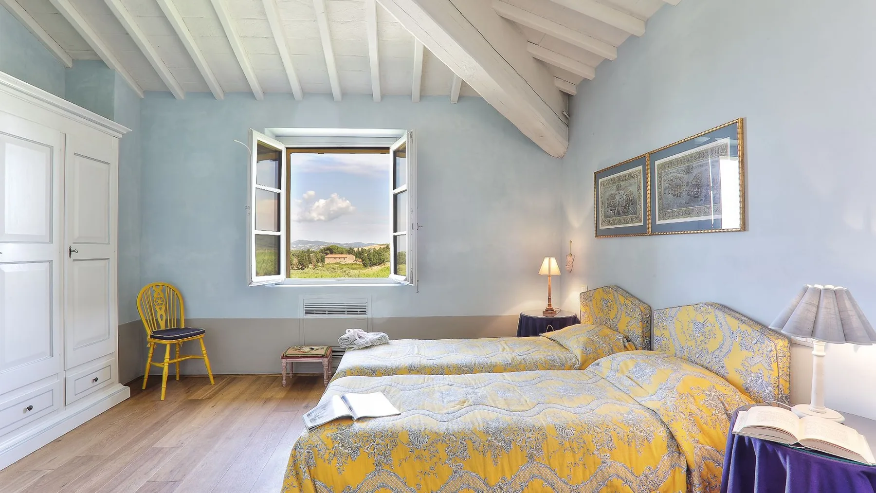 Un dormitorio luminoso con ropa de cama estampada, una ventana abierta y un techo inclinado con vigas.