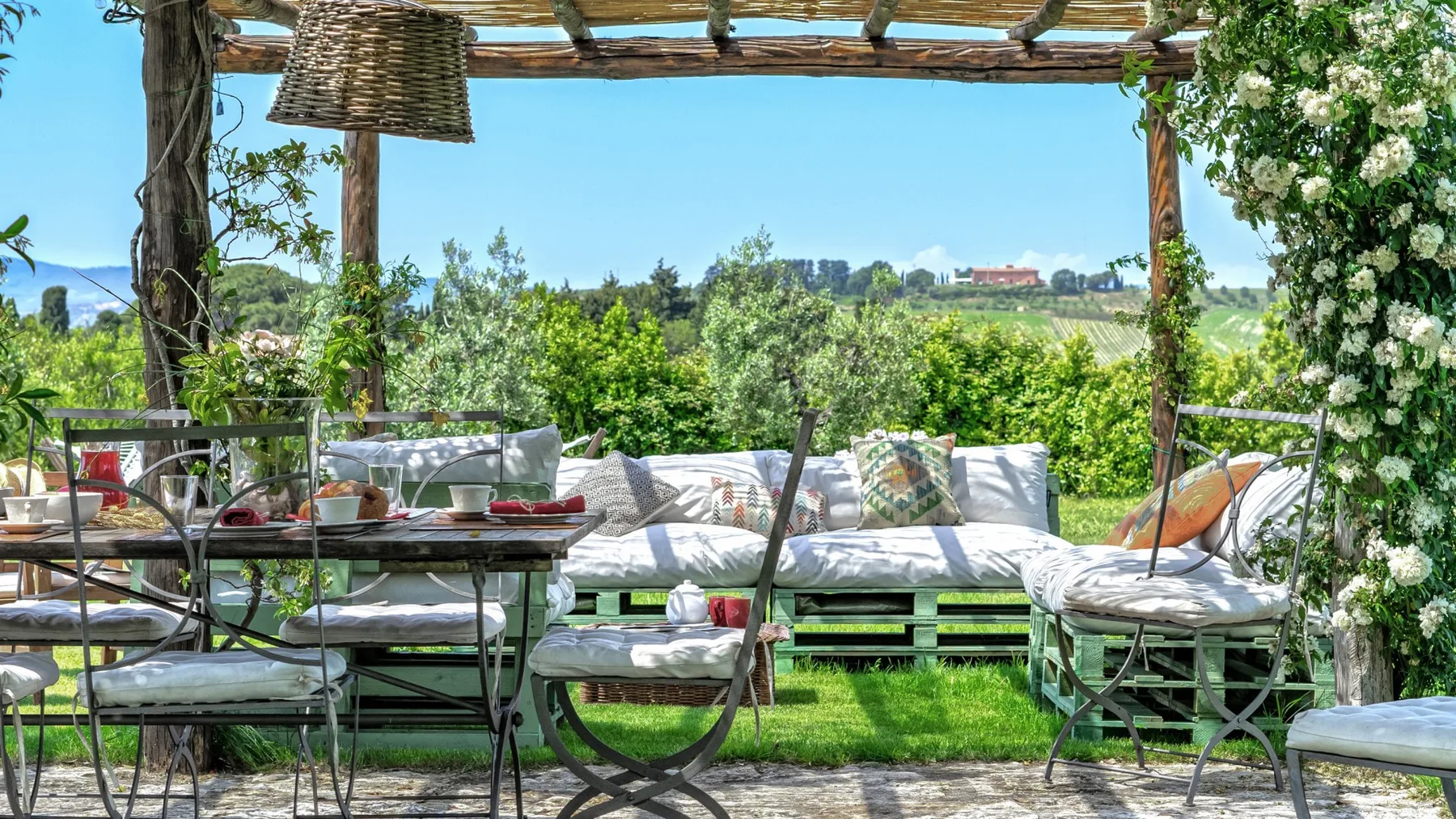 Una zona de estar al aire libre bajo una pérgola de madera, con vistas a campos verdes.