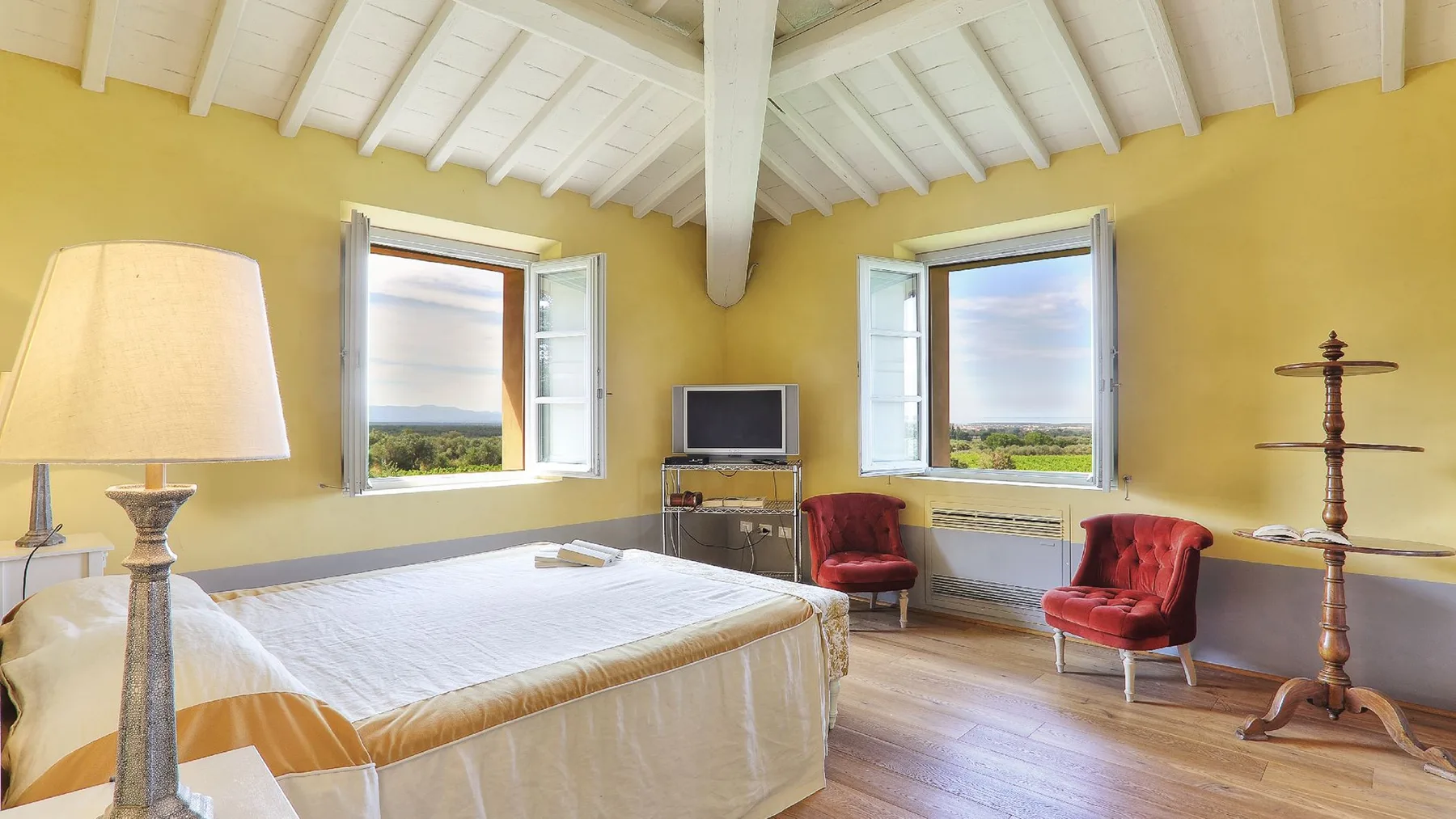 Un dormitorio con una cama, dos sillones rojos y ventanas con vistas al paisaje.