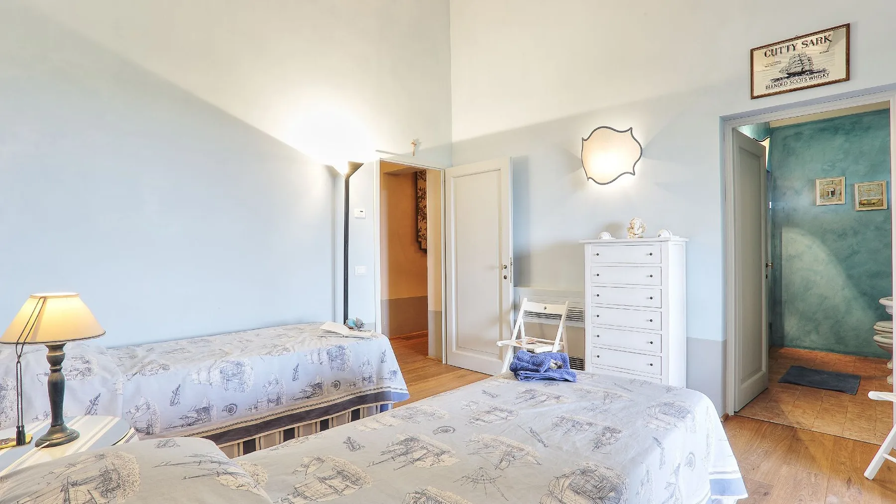 Un dormitorio con camas, una cómoda y una puerta abierta a una habitación contigua.