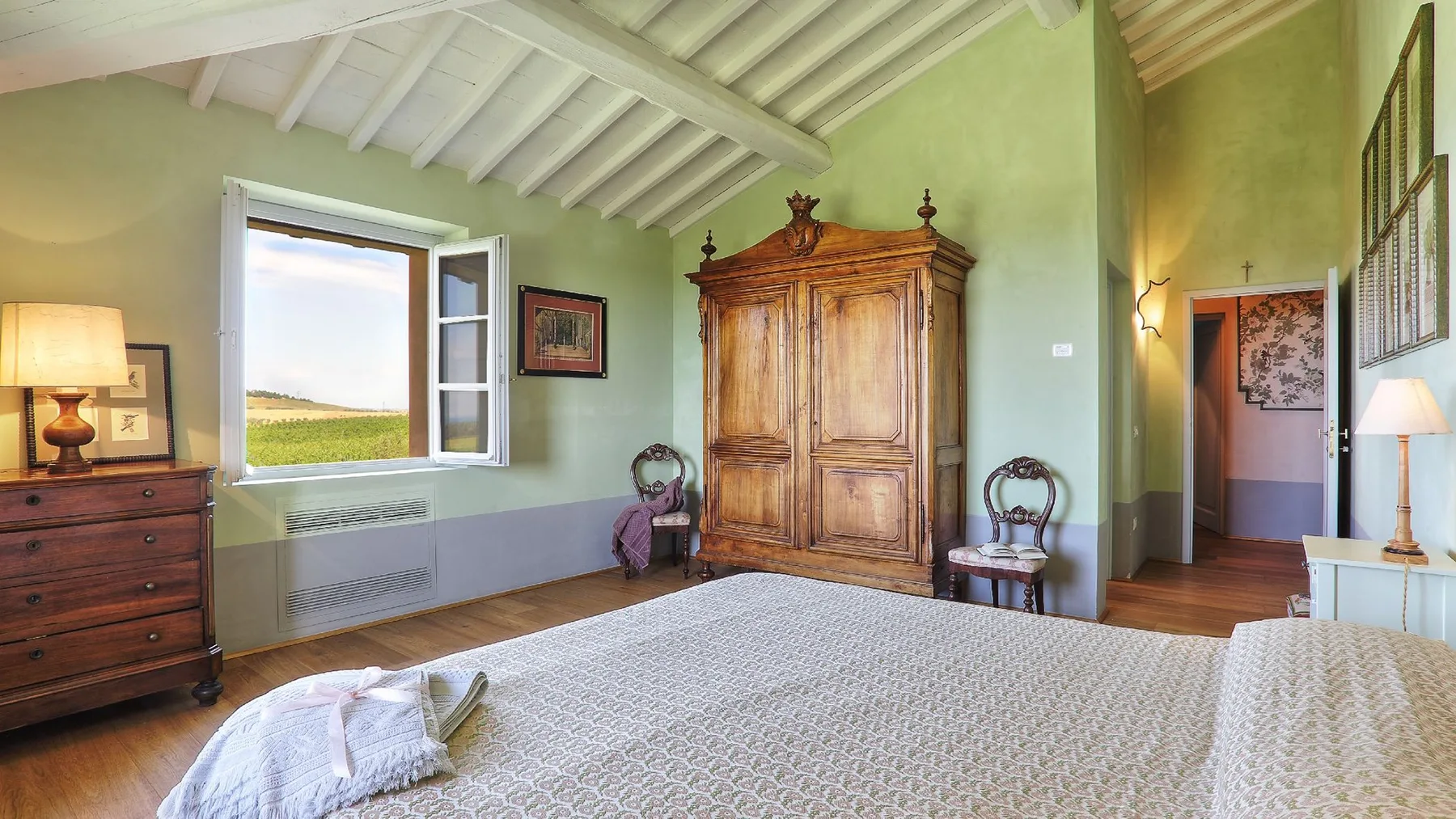 Un dormitorio con un gran armario de madera, una cama y una ventana con vistas a campos abiertos.