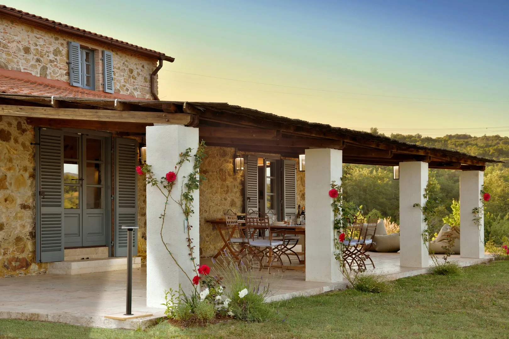 Una casa de piedra con terraza cubierta, asientos al aire libre y plantas con flores.