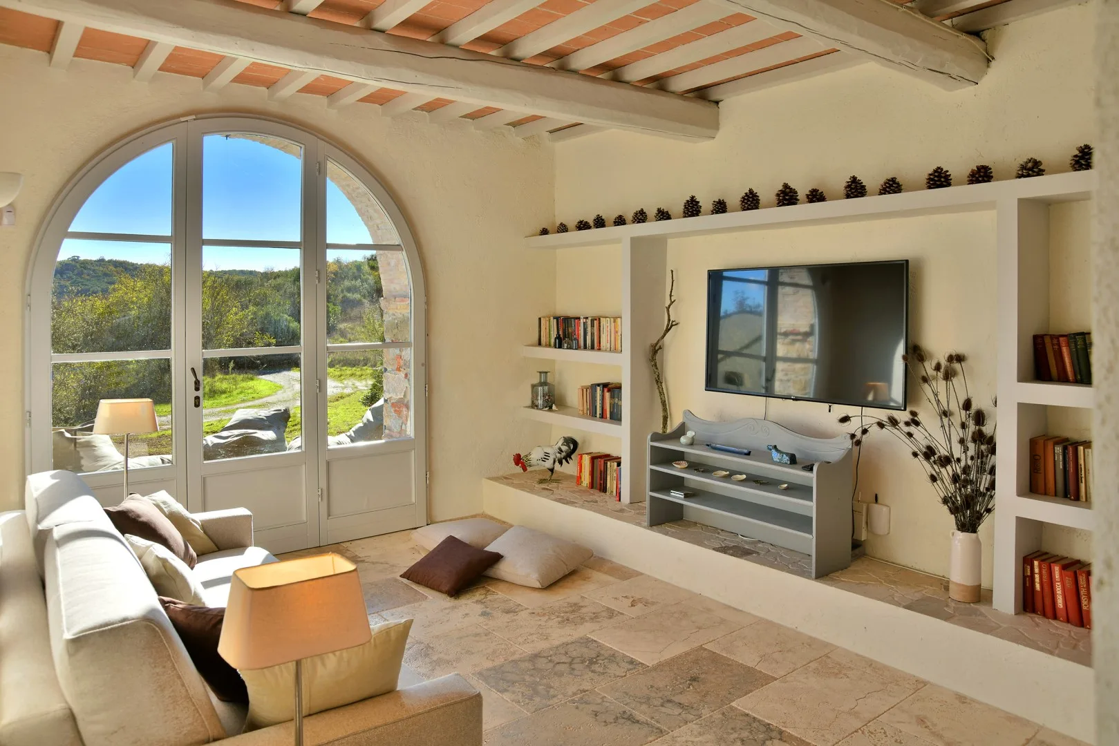Una sala luminosa con una ventana arqueada y un televisor entre estantes empotrados.