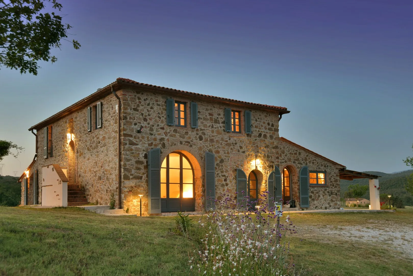 Una casa de piedra se alza en un paisaje de césped, con luz cálida en las ventanas.