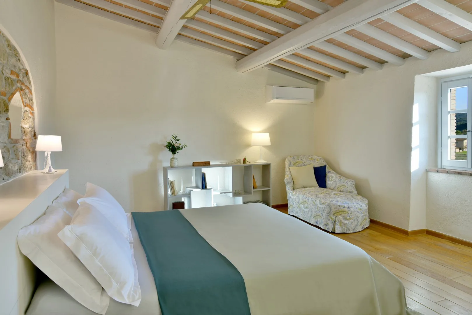 Un dormitorio luminoso con una cama, una pequeña zona de estar y vigas de techo expuestas.