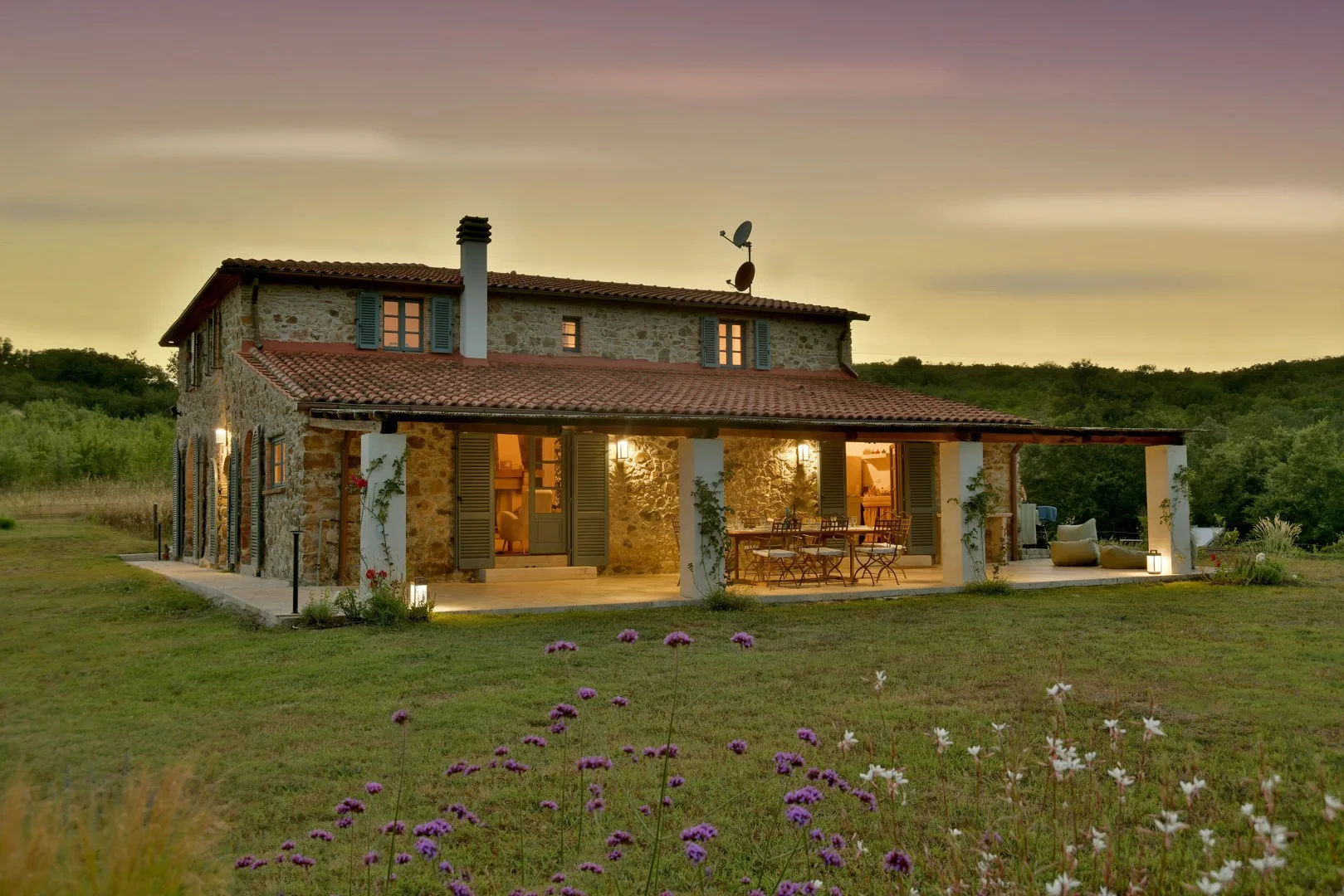 Casa de piedra con tejado de tejas y una zona de estar exterior cubierta.