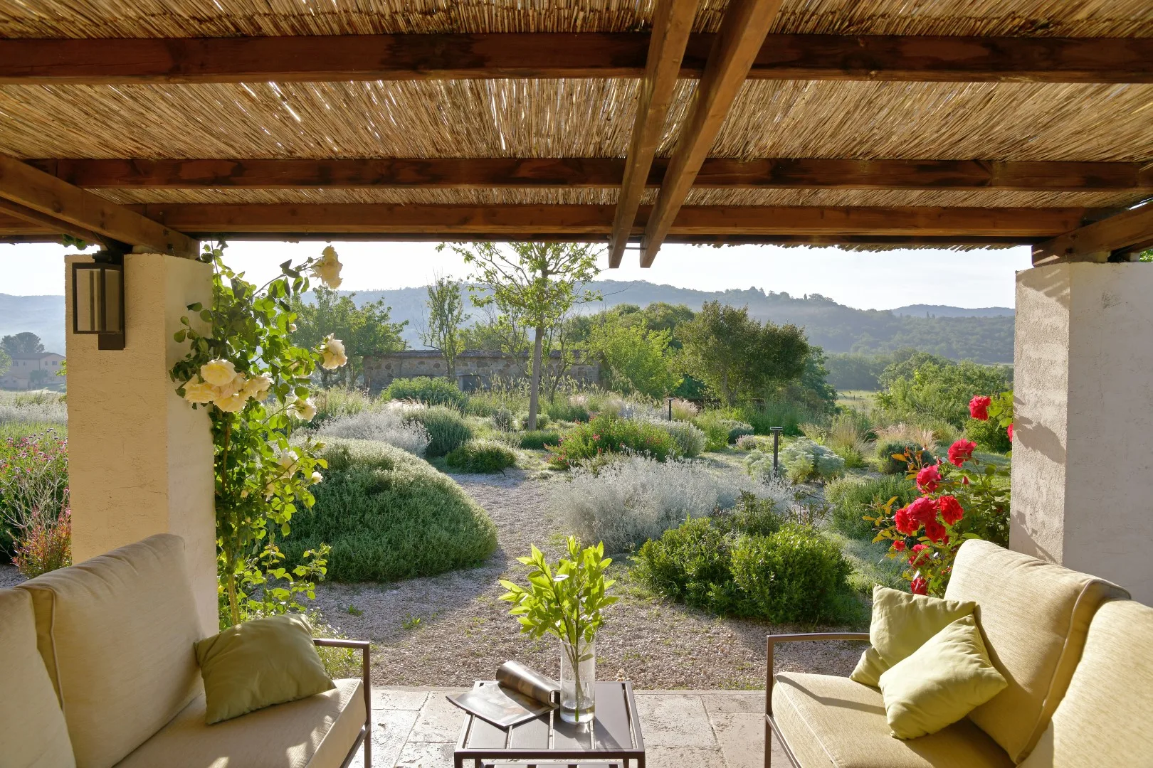 Una zona de estar exterior cubierta da a un jardín ajardinado y colinas lejanas.