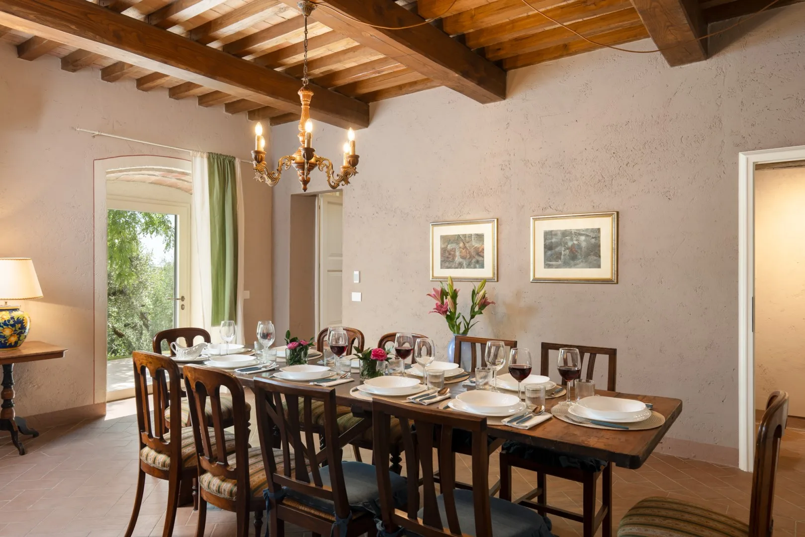 Un comedor con una mesa larga puesta con vajilla bajo vigas de madera a la vista.