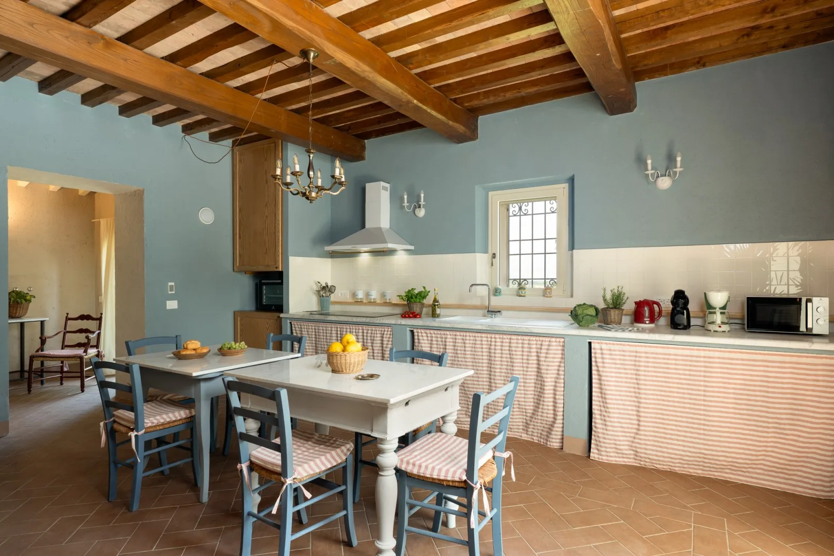 Comedor con una mesa larga y sillas azules junto a una cocina.
