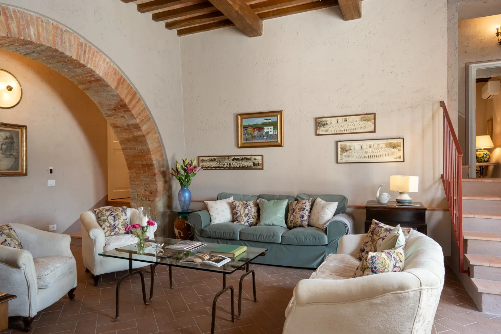 Una sala de estar con un sofá verde, asientos claros y un arco de ladrillo.