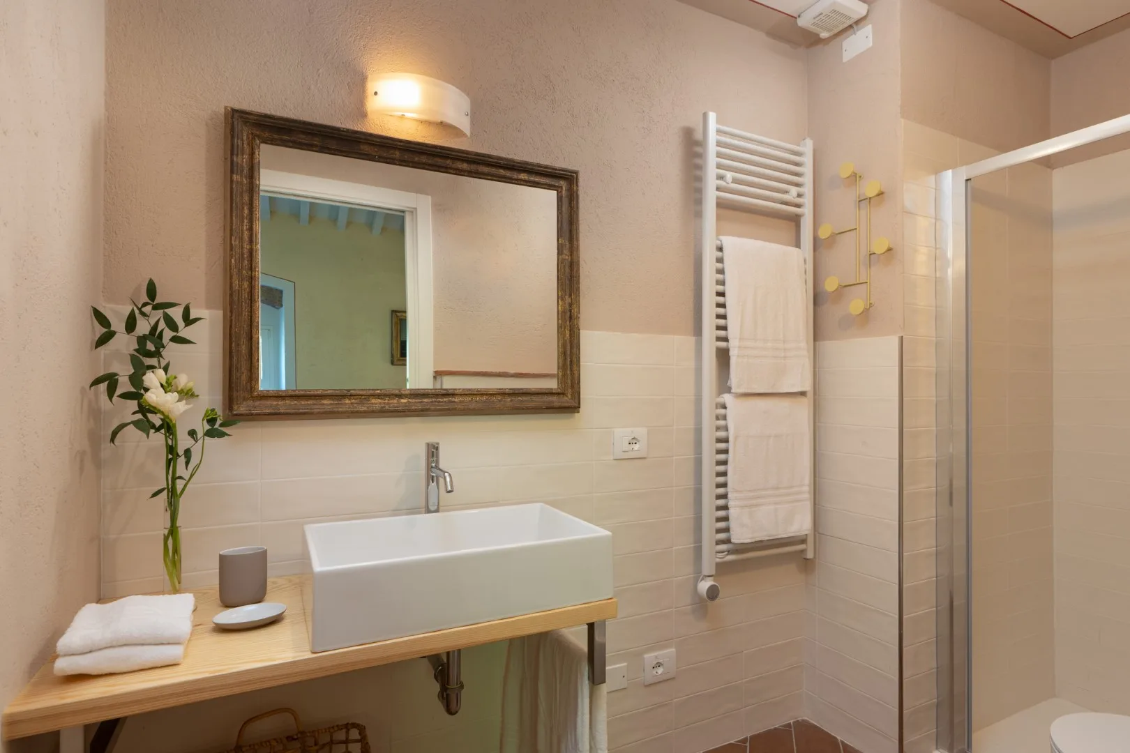 Un baño con lavabo, espejo de pared, toallero calefactor y ducha de vidrio.
