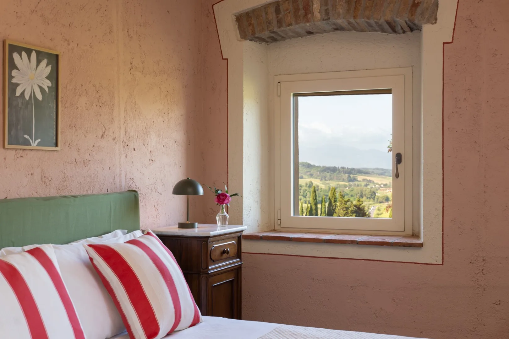 Un dormitorio con una cama junto a una ventana con vistas a un paisaje verde.