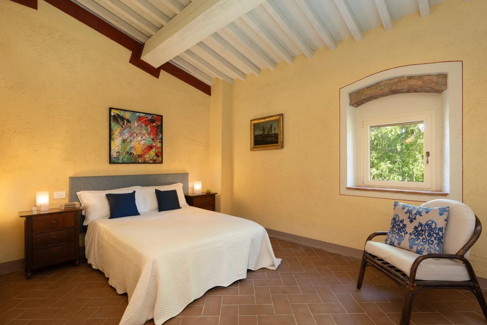 Un dormitorio con una cama doble, mesitas de noche y una ventana con vistas a la vegetación.