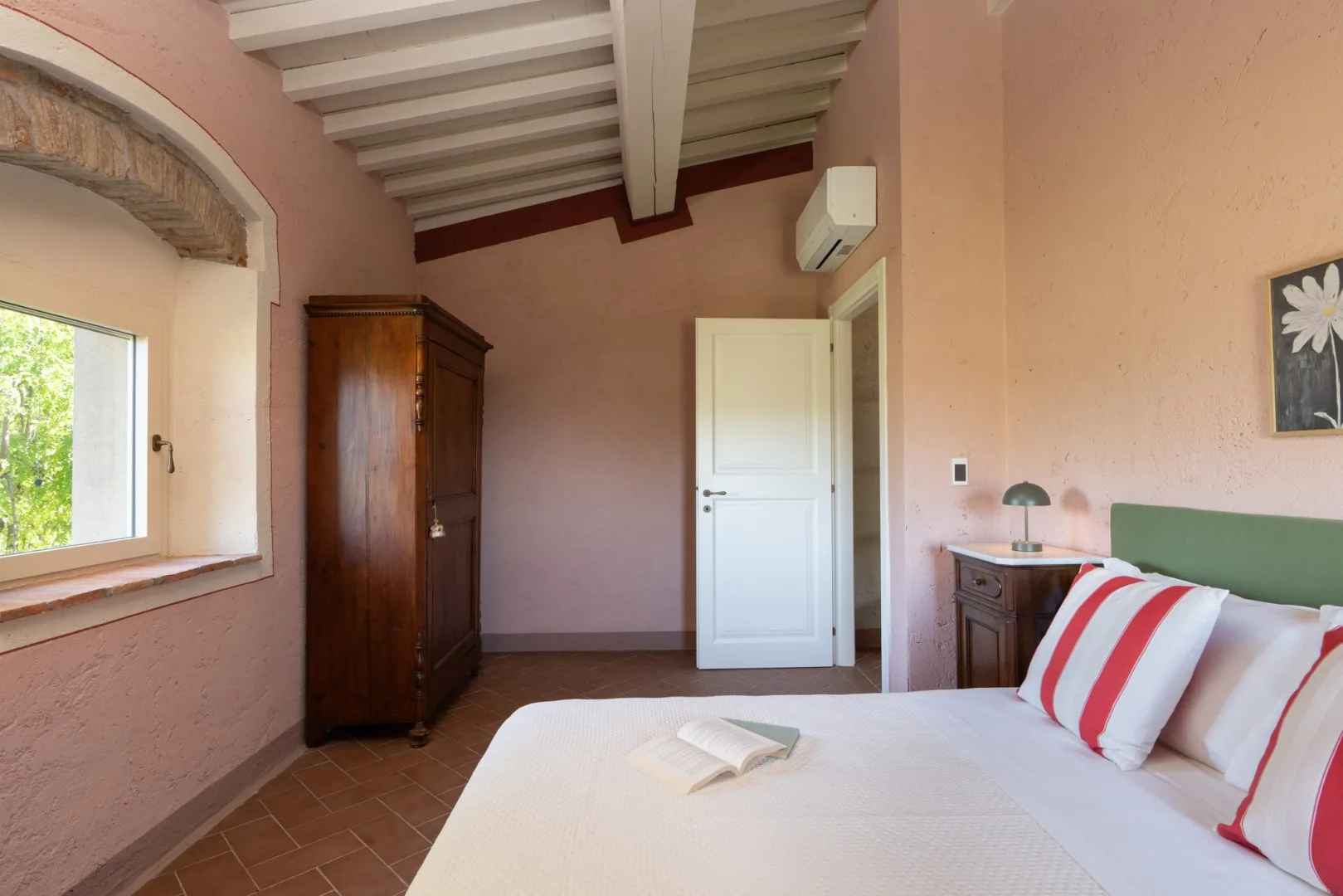 Un dormitorio con una cama blanca, un armario de madera y una ventana con vistas a la vegetación.