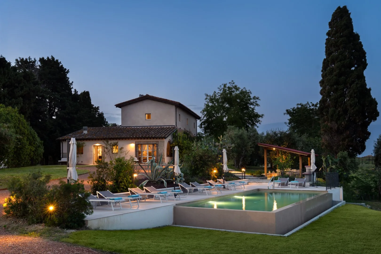 Una casa de campo y una piscina están rodeadas de árboles y asientos de jardín.