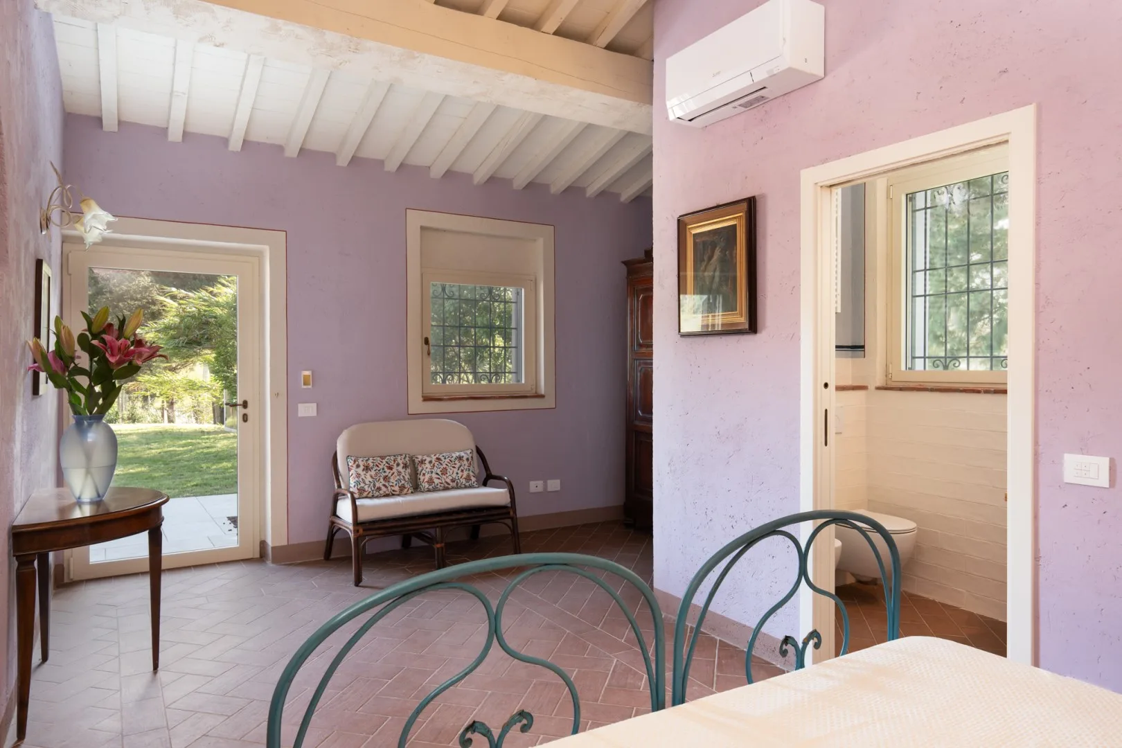 Una habitación de paredes lavanda con una cama y una pequeña zona de estar junto a las ventanas.