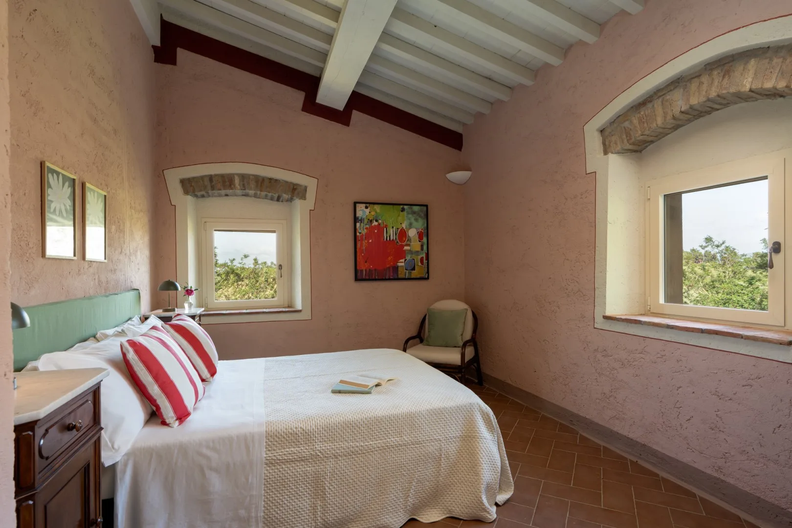 Un dormitorio con una cama, una silla y dos ventanas.